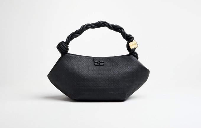 A black handbag sits in front of a white backdrop.