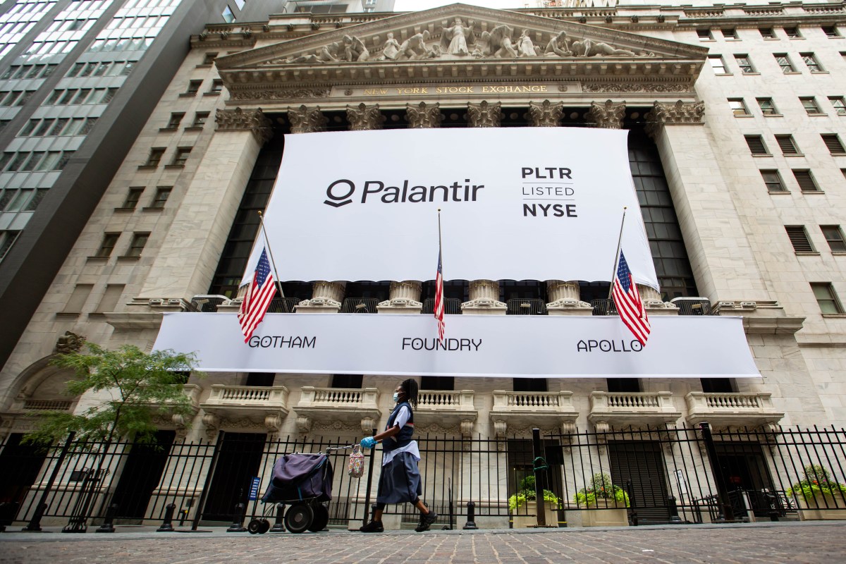 A mail carrier wearing a protective mask passes a banner displaying Palantir Technologies Inc. signage during the company