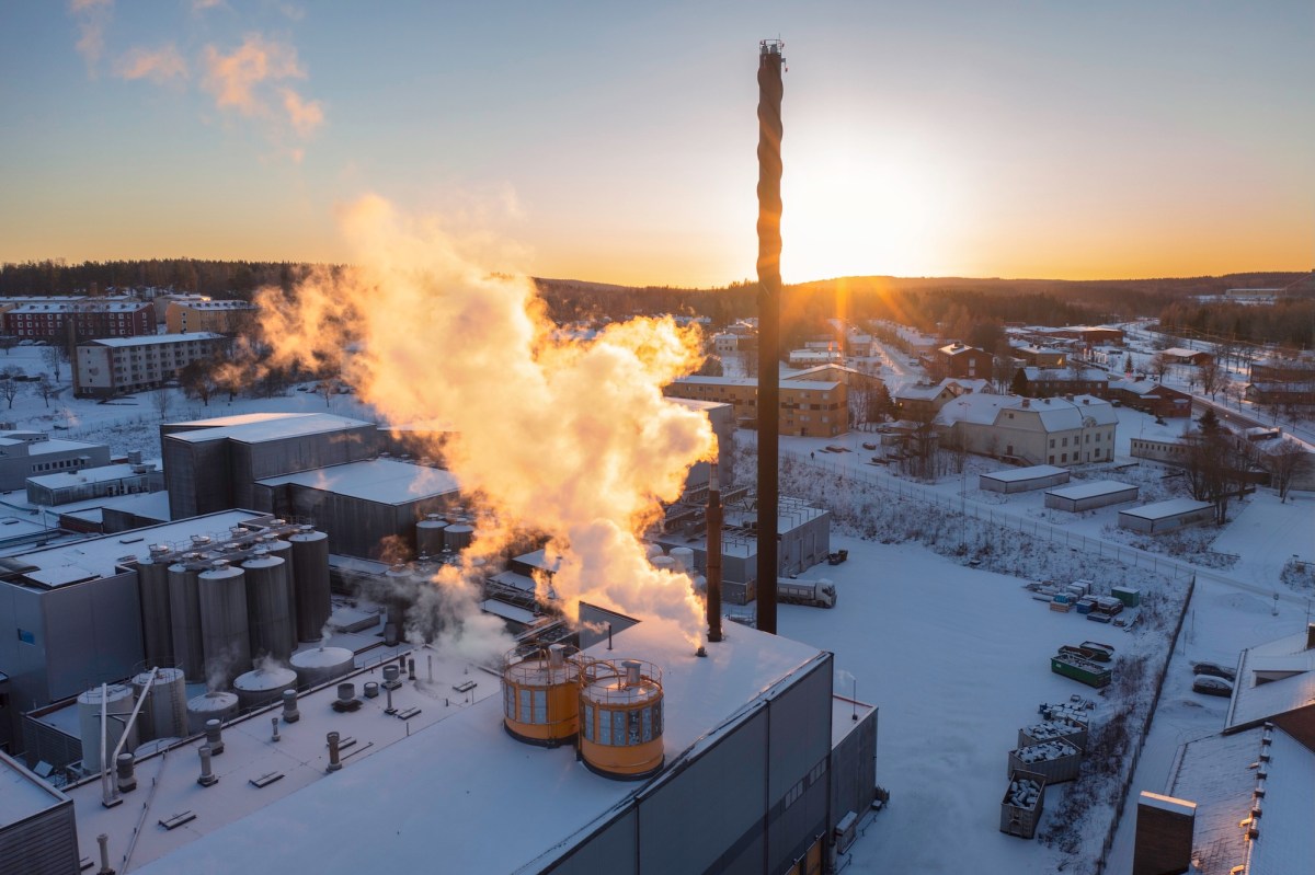 Aerial view of an industrial building in winter with sun lit smoke / steam rising up from the chimneys.